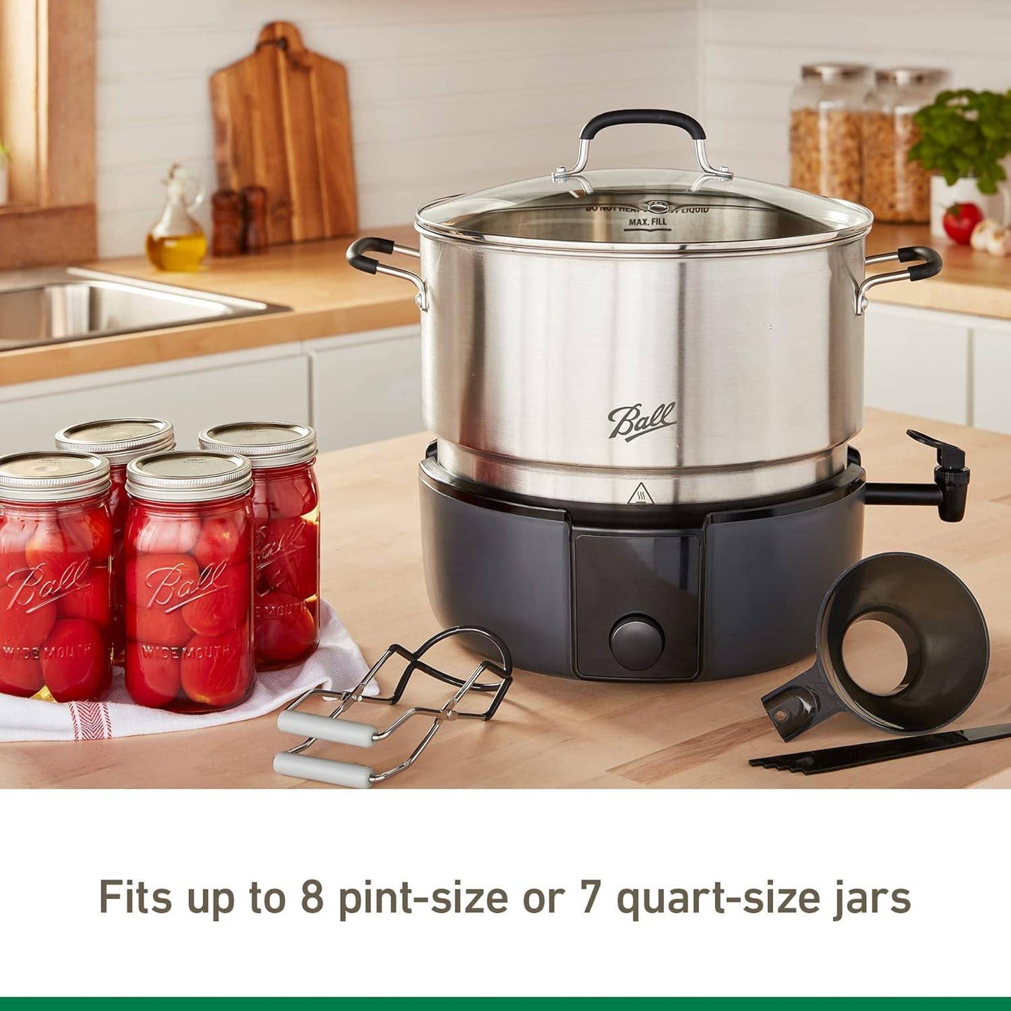 Stainless steel electric water bath canner with clear lid, digital control base, jar lifter, and funnel, set on kitchen counter with jars of preserved tomatoes, ideal for food preservation and canning collections.