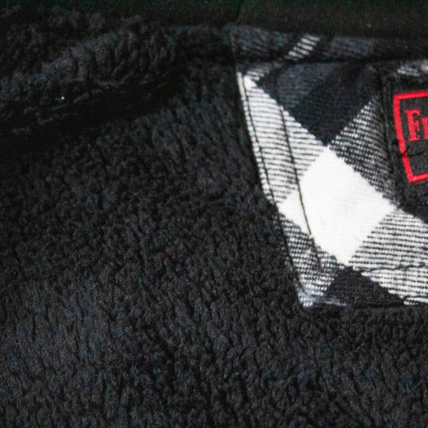 Close-up of handcrafted black sherpa fleece lining next to black and white plaid flannel fabric, showcasing soft texture and quality stitching in clothing and health & wellness collections.