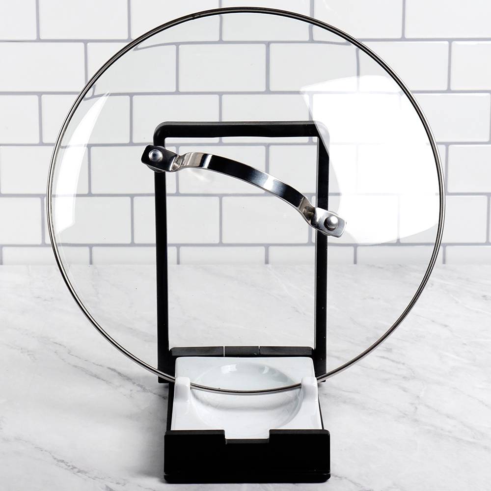 Two-in-one kitchen gadget with black plastic frame and white porcelain rest holding a glass pot lid upright, designed to keep cooking areas tidy in Kitchen & Food and Kitchen Gadgets collections.