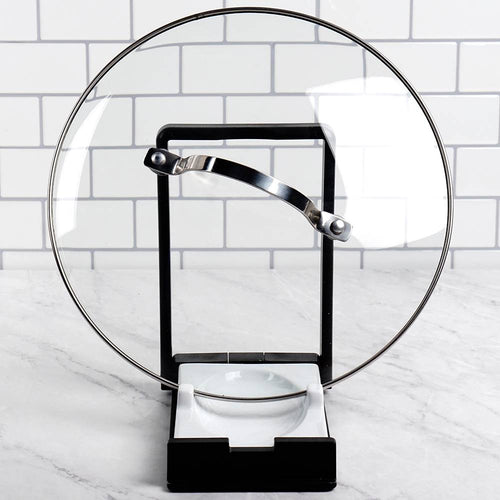 Two-in-one kitchen gadget with black plastic frame and white porcelain rest holding a glass pot lid upright, designed to keep cooking areas tidy in Kitchen & Food and Kitchen Gadgets collections.