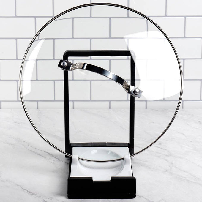 Two-in-one kitchen gadget with black plastic frame and white porcelain rest holding a glass pot lid upright, designed to keep cooking areas tidy in Kitchen & Food and Kitchen Gadgets collections.