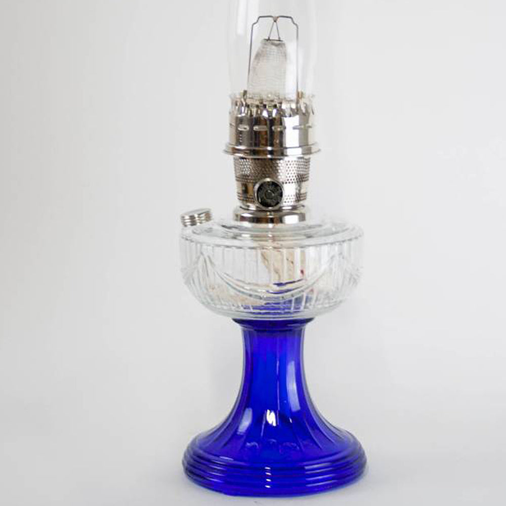 Unique handcrafted oil lamp with a sweeping clear glass font and vibrant cobalt glass base, featuring a nickel burner, ideal for Lamps & Lighting, Oil Lamps, Table Lamps, Best Sellers, and Promo Eligible collections.