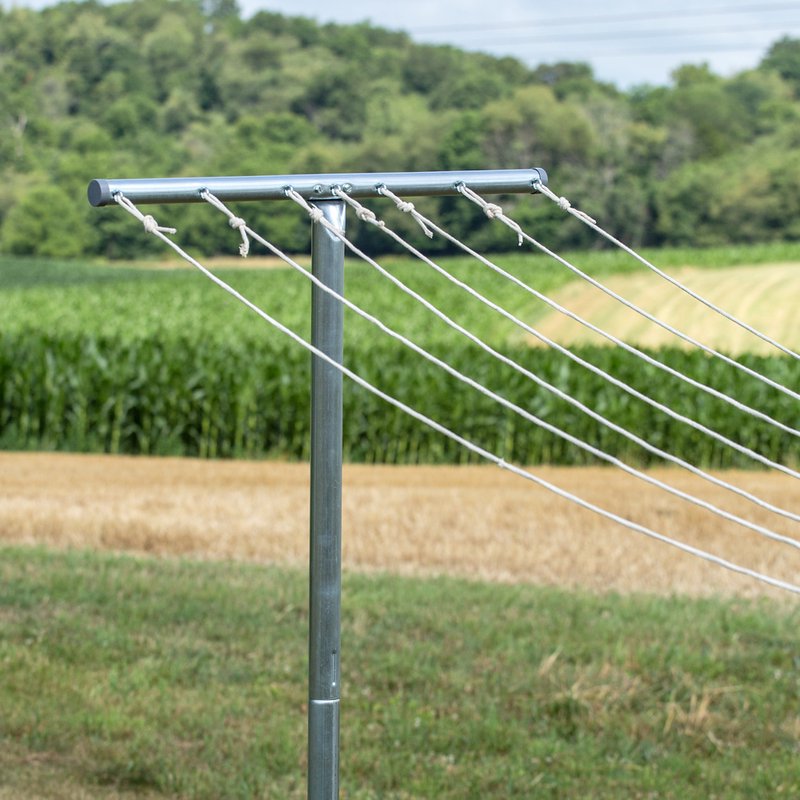Metal T-post clothes dryer with multiple white drying lines stretched across a rural outdoor setting, suitable for Home & Decor, Laundry Supplies, Clothesline and Drying Accessories collections.