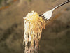 Fork holding a tangled bite of homemade sauerkraut strands against a blurred neutral background, illustrating traditional fermentation and preserving techniques in farm and garden culture.