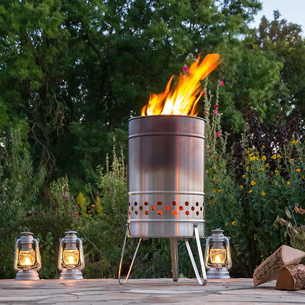 Stainless steel outdoor cooking stove with vibrant flames burning inside, surrounded by four vintage-style oil lanterns on a stone patio, ideal for camping and garden use.