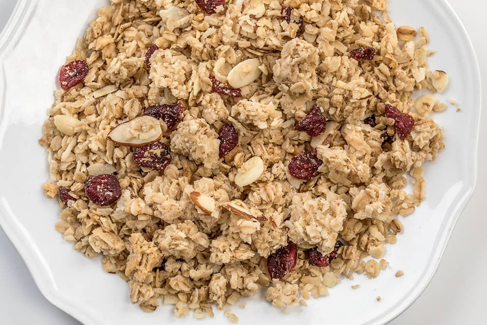Close-up of wholesome granola with oats, sliced almonds, and dried cranberries on a white plate, handcrafted and made in USA, perfect for Kitchen & Food and Snacks collections.