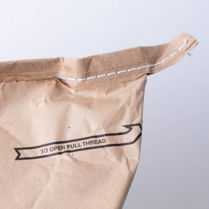 Close-up of the top corner of a stitched brown paper bag with an instruction to pull the thread for opening, suitable for pantry, food, and emergency supplies collections.