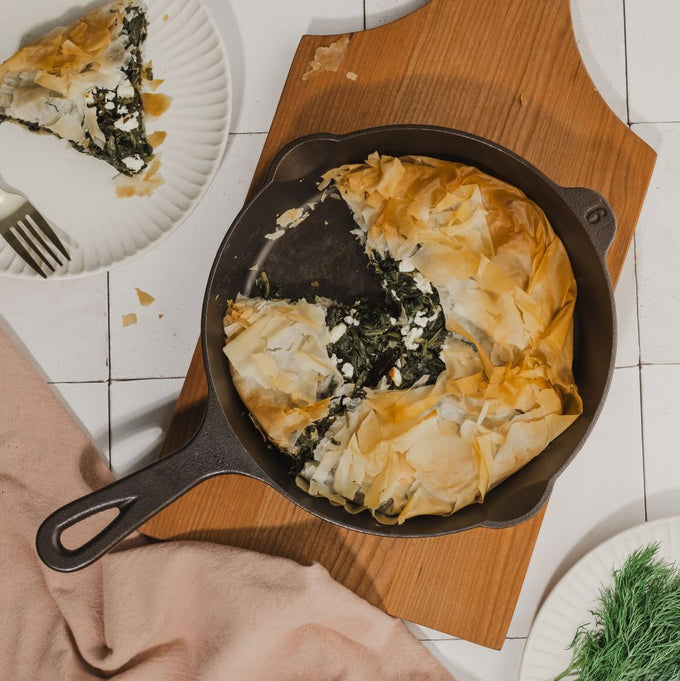 Handcrafted cast iron skillet with flaky spinach and cheese pie, resting on a wooden cutting board, suitable for Kitchen & Food, Cast Iron, USA Made, Camping, and Best Sellers collections.