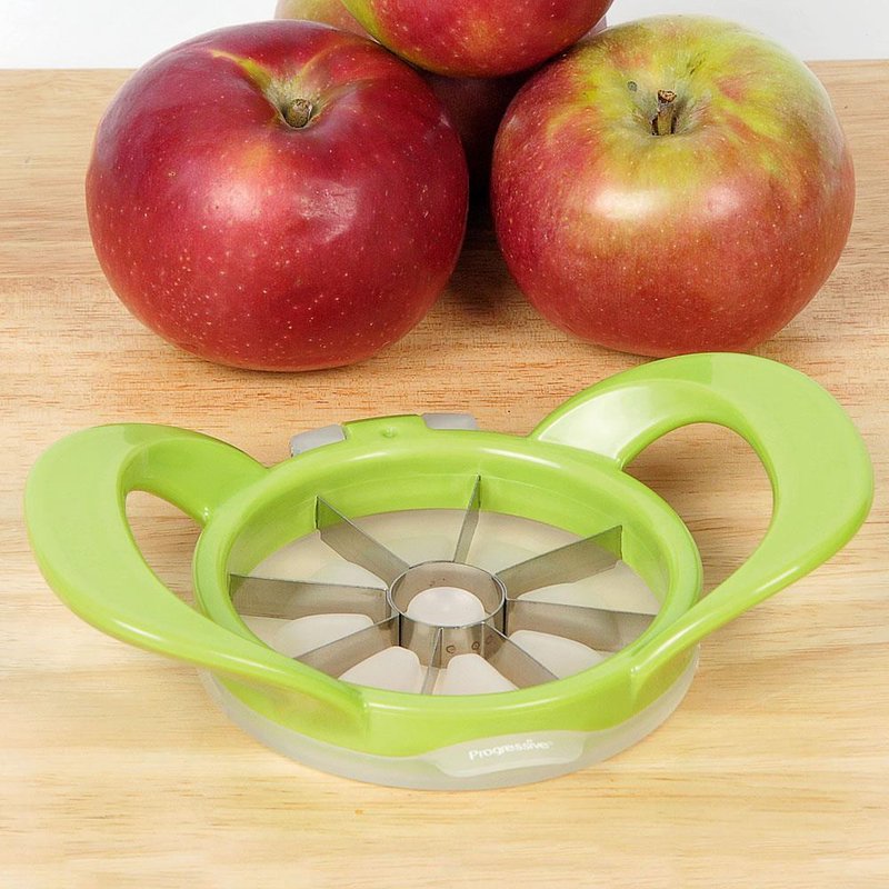 Green-handled apple wedge cutter with stainless steel blades placed on a wooden surface beside three red apples, perfect for food prep and apple harvest collections.