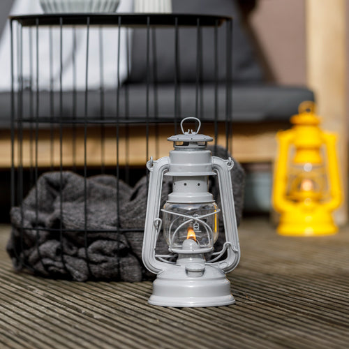 Handcrafted galvanized oil lantern with thermal heat-resistant SUPRAX globe glowing softly on wooden decking, showcased with a rustic wire basket and yellow lantern in background, ideal for Lamps & Lighting, Camping, and Emergency Supplies collections.