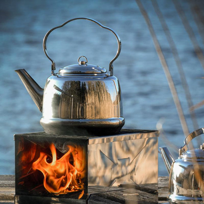 Shiny stainless steel teakettle with a curved bent handle heating over an outdoor fire, suitable for Farm, Garden & Tool, Kitchen & Food, Camping, Brewing Coffee and Tea, Best Sellers, and Promo Eligible collections.