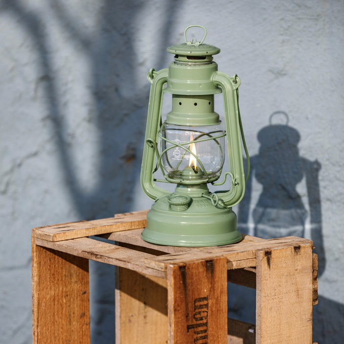 Handcrafted pale green galvanized oil lantern with thermal heat-resistant globe burning outdoors on rustic wooden crate, ideal for Lamps & Lighting, Camping, Emergency Supplies collections.