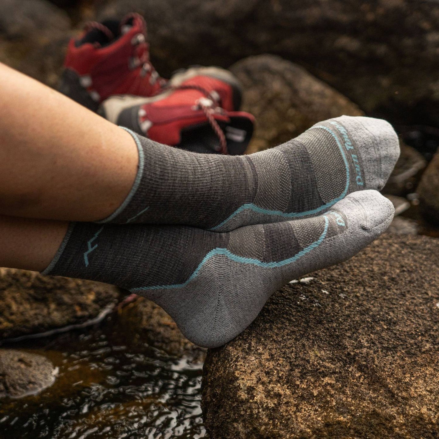 Pair of lightweight breathable hiking socks with mesh panels and smooth ribbing in gray tones, worn outdoors near rocks, ideal for camping, health & wellness, and USA made collections.