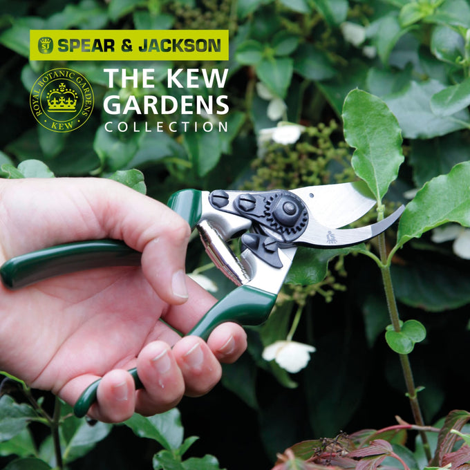 Close-up of a hand using heavy-duty left-handed bypass pruners with green ergonomic handles and a notched blade to trim thick garden stems, featured in Farm, Garden & Tool, Garden Accessories, Lawncare, Best Sellers, and Promo Eligible collections.