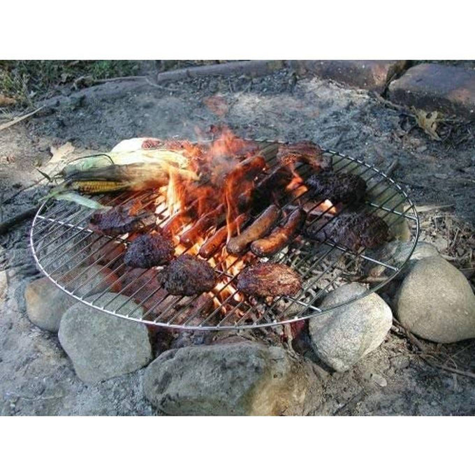 Round chrome-plated steel grill grate placed over a stone fire ring with sausages, grilled corn, and burgers cooking on an open campfire, suited for outdoor grilling in Camping and Farm, Garden & Tool collections.