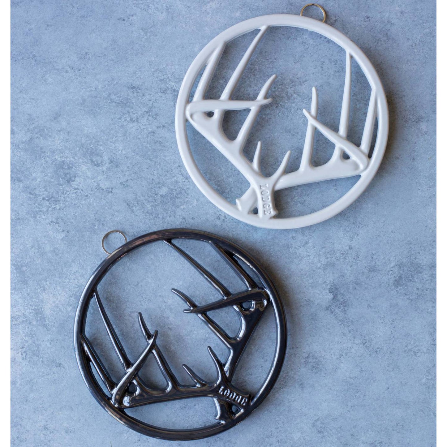 Two enamel antler design trivets in black and white with built-in hangers and rubber feet, ideal for Kitchen & Food, Dinnerware, Storage and Serving, Best Sellers, and Promo Eligible collections.