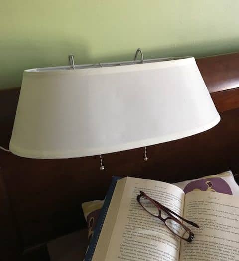 Ivory double headboard lamp with two pull chains and hanging hooks, mounted on a wooden headboard above an open book and reading glasses, ideal for Home & Decor and Lamps & Lighting collections.