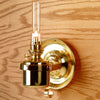 Handcrafted brass gimbaled oil lamp mounted on a wood wall, featuring a clear glass chimney and steady flame, ideal for lamps & lighting, oil lamps, and table lamp collections.