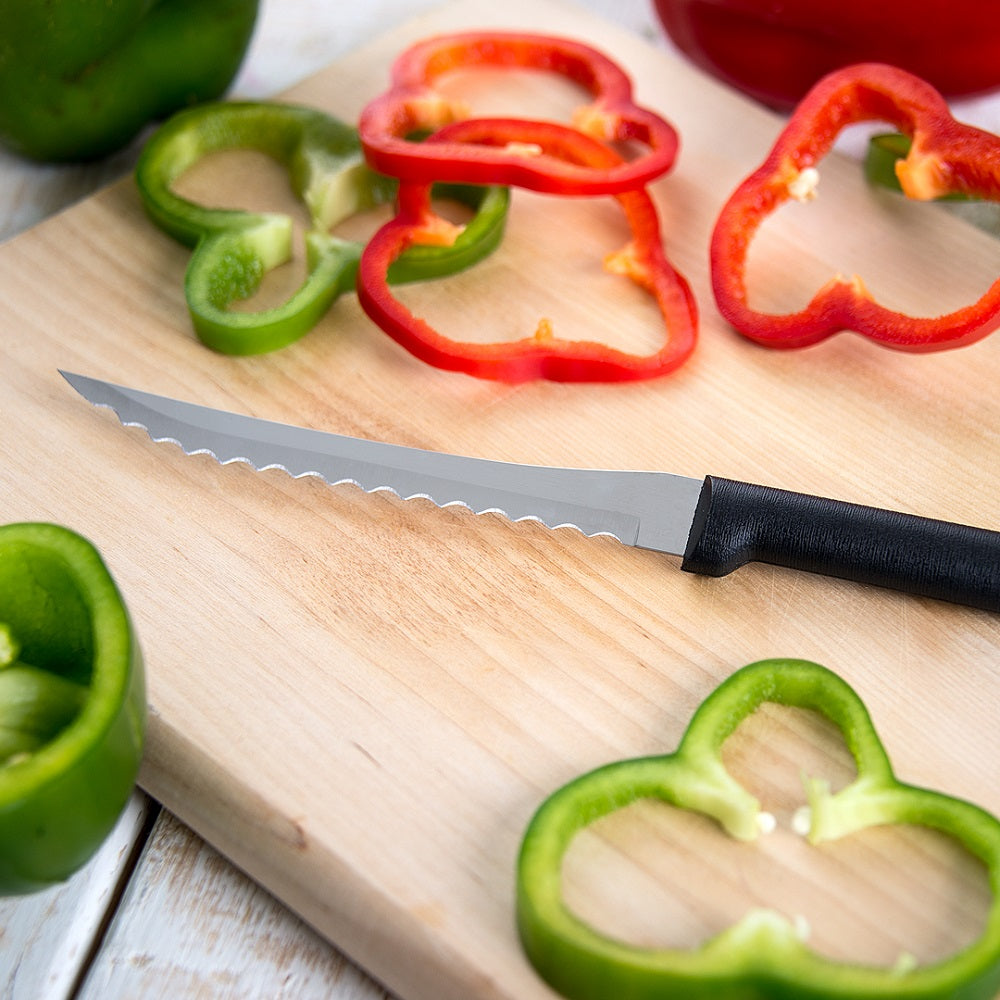 Serrated tomato slicer with hand-sharpened high carbon stainless steel blade and black handle resting on wooden cutting board with red and green pepper slices, perfect for kitchen food prep and USA made collections.
