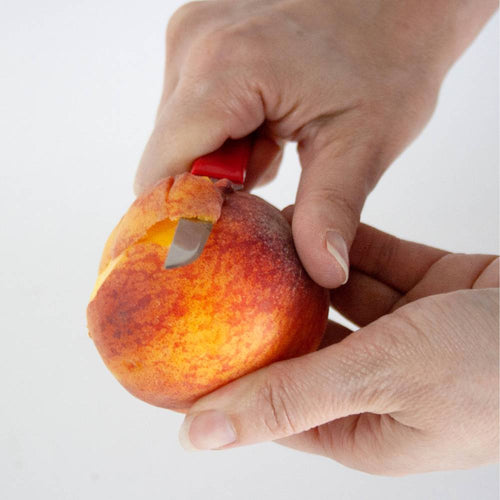 Handcrafted flexible paring knife with a sharp blade and red handle peeling a ripe peach, ideal for precise fruit preparation in Farm, Garden & Tool and Kitchen & Food collections.