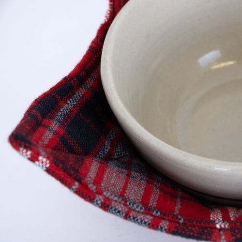 Close-up of a handcrafted red and black plaid cotton cozy gently cradling a beige ceramic bowl, ideal for protecting hands and tabletops, featured in Kitchen & Food, Kitchen Textiles, Storage and Serving, Best Sellers, and Promo Eligible collections.