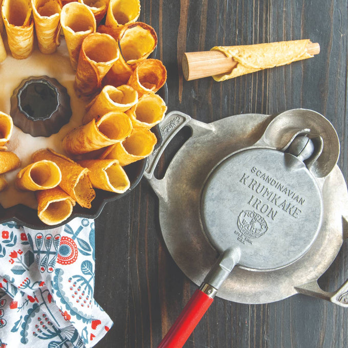 Handcrafted stovetop krumkake iron with aluminum base and red wooden handle, made in USA, shown with rolled cookies and traditional baking accessories, ideal for Kitchen & Food and Baking Supplies collections.