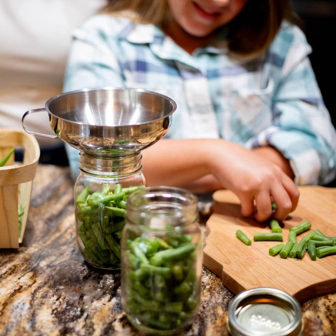 Stainless steel funnel with removable spout guiding green beans into a jar on a kitchen counter, perfect for food preservation, canning, and cooking helpers collections.