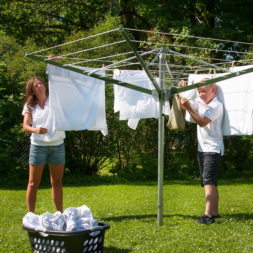 Two people hanging laundry on a large rotating clothes dryer outdoors on a sunny day, set on green grass with trees in the background, ideal for Laundry Supplies and Home & Decor collections.