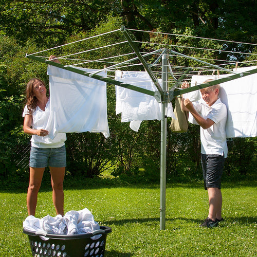 Two people hanging laundry on a large rotating clothes dryer outdoors on a sunny day, set on green grass with trees in the background, ideal for Laundry Supplies and Home & Decor collections.