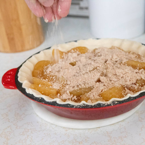 Handcrafted cast iron pie pan with crimped edges and red exterior, filled with pie filling and streusel topping being sprinkled, ideal for Kitchen & Food, Cookware, Cast Iron, Baking Supplies, Best Sellers, and Promo Eligible collections.
