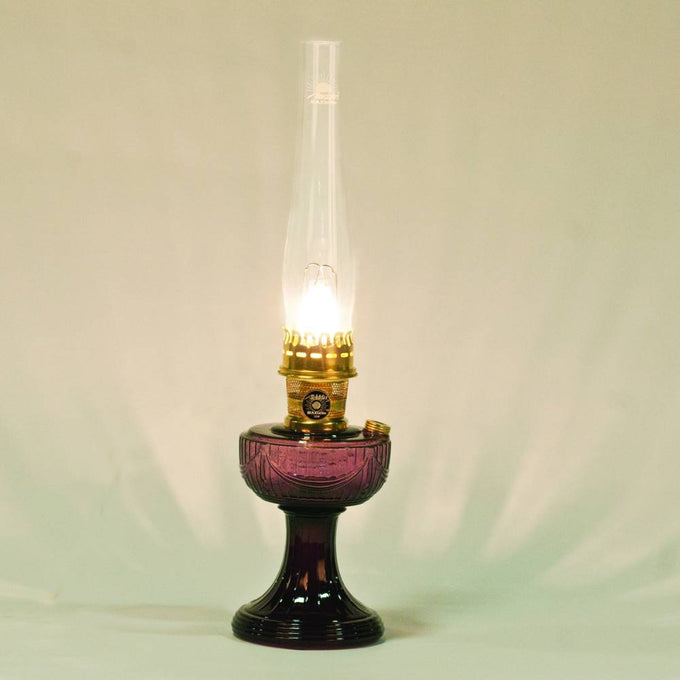 Lit oil lamp featuring a purple glass base and tall clear chimney, showcasing a vintage-inspired design ideal for Farm, Garden & Tool, Lamps & Lighting, and Homesteading collections.