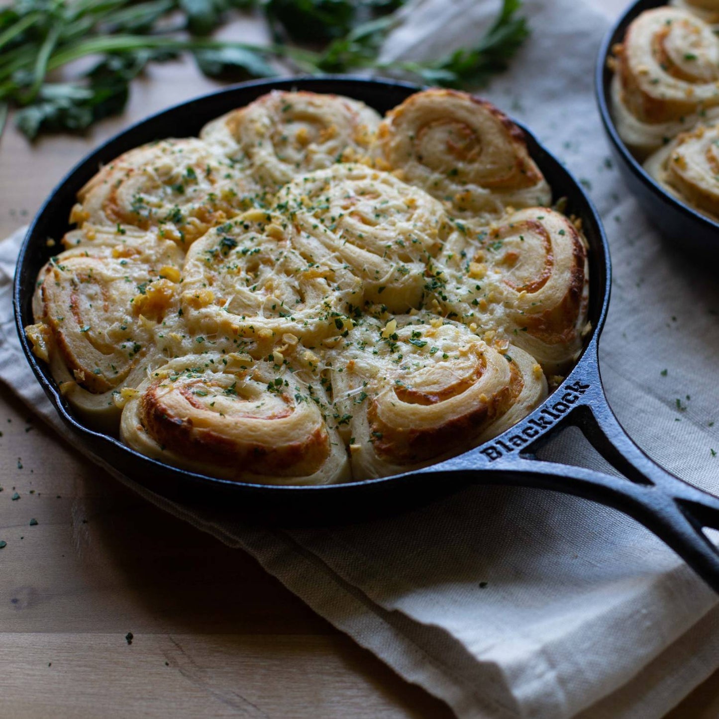 Lodge Blacklock cast iron skillet filled with freshly baked savory rolls topped with melted cheese and herbs, set on a linen cloth in a rustic kitchen setting, ideal for Kitchen & Food and Cookware collections.