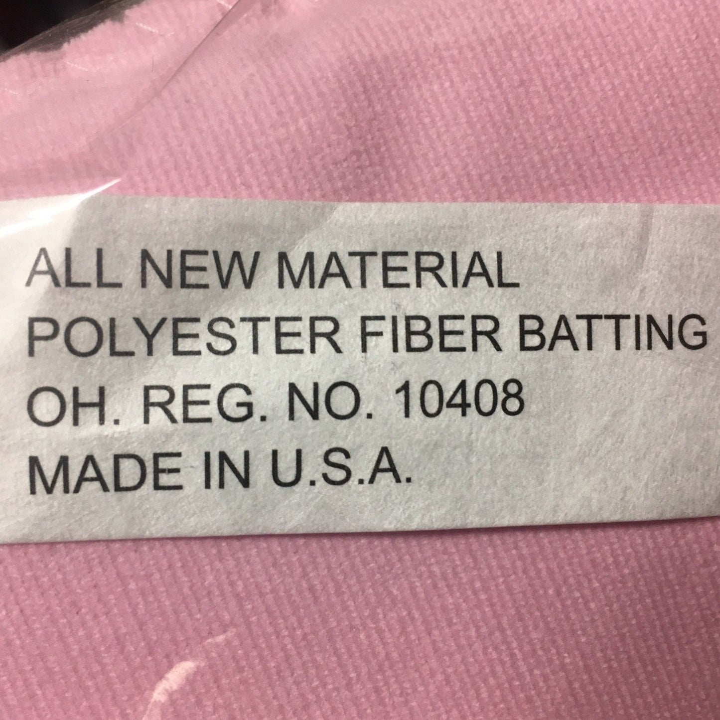 Close-up of a label on pink fabric stating the product is made in the USA with all new polyester fiber batting, highlighting quality and craftsmanship for children's toys and Amish Made collections.