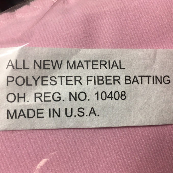 Close-up of a label on pink fabric stating the product is made in the USA with all new polyester fiber batting, highlighting quality and craftsmanship for children's toys and Amish Made collections.
