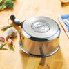 Shiny stainless steel saucepan with heavy-duty base embossed with branding, resting upside down on a wooden kitchen counter surrounded by garlic and fresh herbs, part of cookware collections.