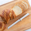 Handcrafted serrated bread knife with a sharp stainless steel blade and smooth handle, made in USA, slicing through soft and crusty bread on a wooden cutting board, ideal for Kitchen & Food and Bread Making Supplies collections.