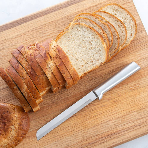 Handcrafted serrated bread knife with a sharp stainless steel blade and smooth handle, made in USA, slicing through soft and crusty bread on a wooden cutting board, ideal for Kitchen & Food and Bread Making Supplies collections.