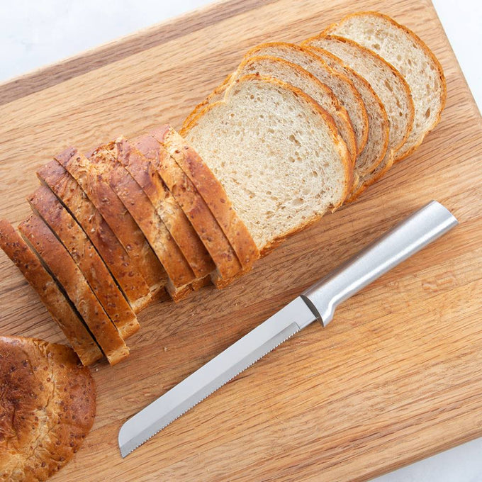 Handcrafted serrated bread knife with a sharp stainless steel blade and smooth handle, made in USA, slicing through soft and crusty bread on a wooden cutting board, ideal for Kitchen & Food and Bread Making Supplies collections.