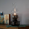 Handcrafted wall-mounted oil lamp with a polished pewter-like finish and clear ribbed glass chimney, casting a warm glow, featured in Lamps & Lighting and Oil Lamps collections.