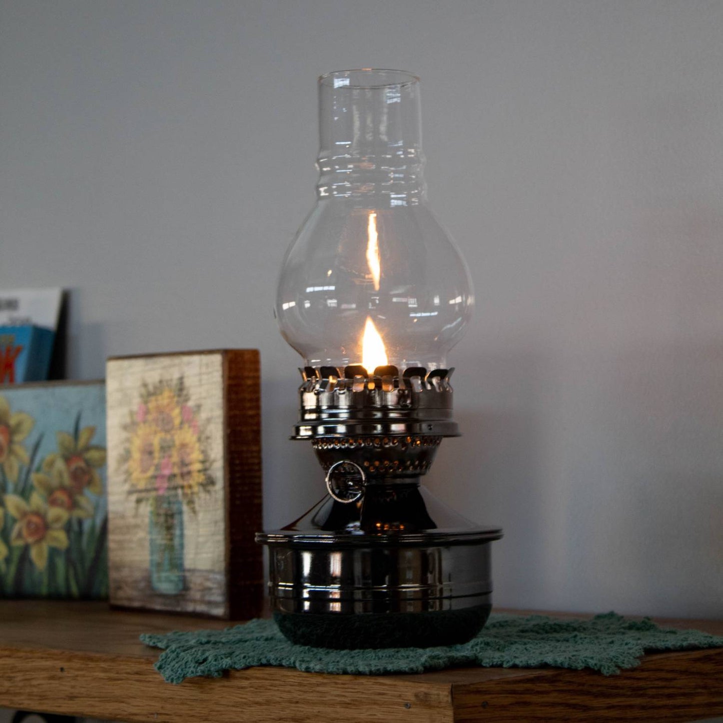 Handcrafted wall-mounted oil lamp with a polished pewter-like finish and clear ribbed glass chimney, casting a warm glow, featured in Lamps & Lighting and Oil Lamps collections.