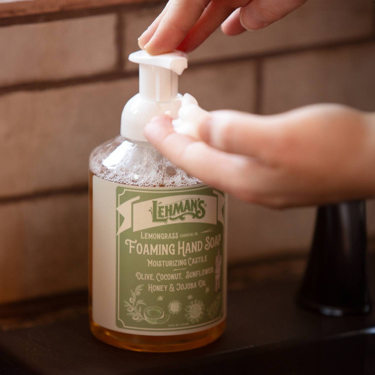 Hand pressing pump to dispense foaming hand soap with natural moisturizing ingredients including olive, coconut, sunflower, honey, and jojoba oils, made in USA, featured in Health & Wellness and Grooming collections.