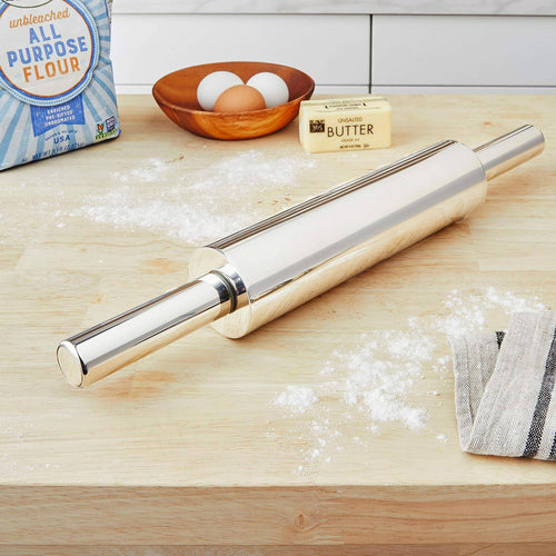 Sleek stainless steel rolling pin with nylon bearings resting on a floured wooden counter alongside flour, eggs in a wooden bowl, and unsalted butter, featured in Kitchen & Food, Cookware, Baking Supplies, and Best Sellers collections.
