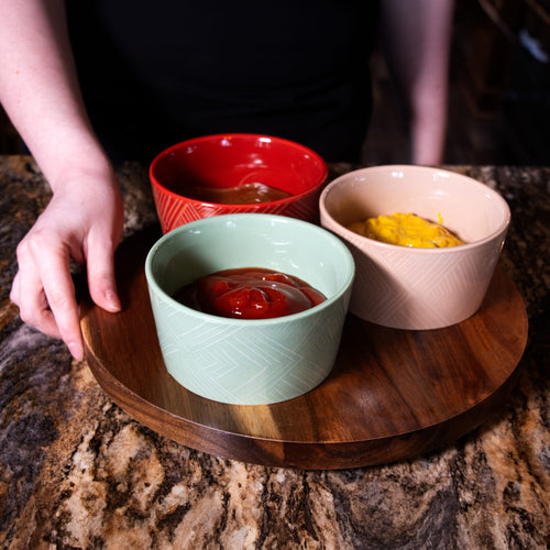 Round wooden Lazy Susan turntable holding three ceramic condiment bowls in red, beige, and green filled with sauces, featured in Kitchen & Food, Storage and Serving collections.