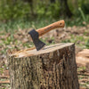 Hand-forged Swedish steel hatchet with a curved wooden handle embedded in a tree stump, crafted for camping, farm, and woodcutting tasks, featuring a protective leather sheath option.
