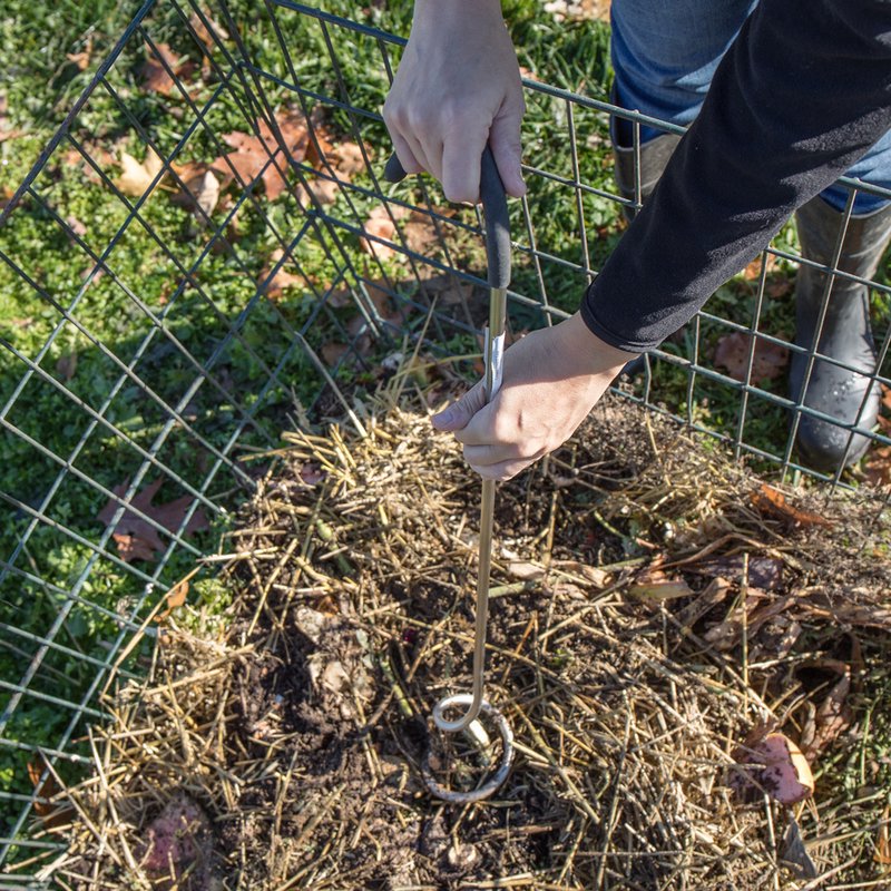 Hands using a Compost Crank Twist with stainless steel spiral and cushioned handle to aerate and mix compost inside a wire compost bin outdoors, part of Farm, Garden & Tool and USA Made collections.