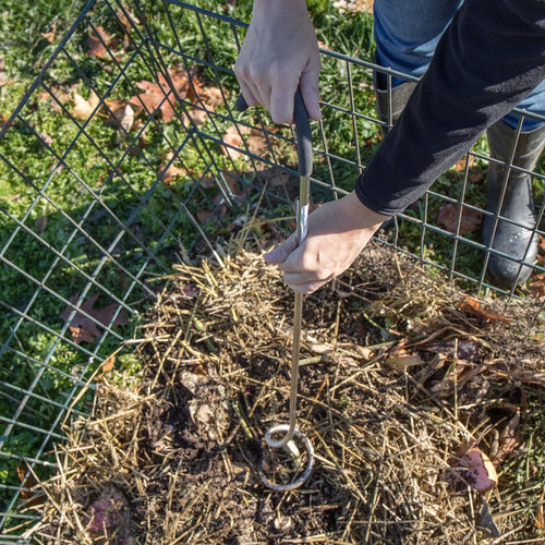 Hands using a Compost Crank Twist with stainless steel spiral and cushioned handle to aerate and mix compost inside a wire compost bin outdoors, part of Farm, Garden & Tool and USA Made collections.