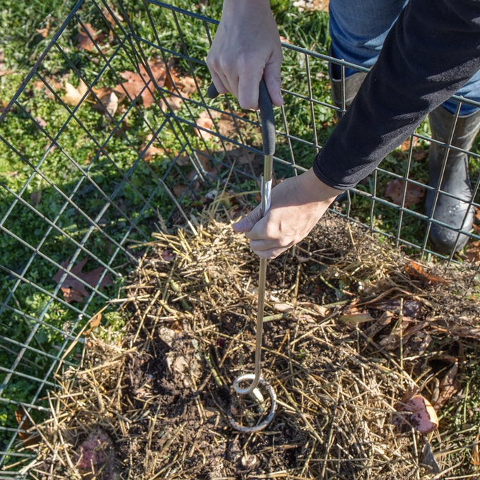 Hands using a Compost Crank Twist with stainless steel spiral and cushioned handle to aerate and mix compost inside a wire compost bin outdoors, part of Farm, Garden & Tool and USA Made collections.
