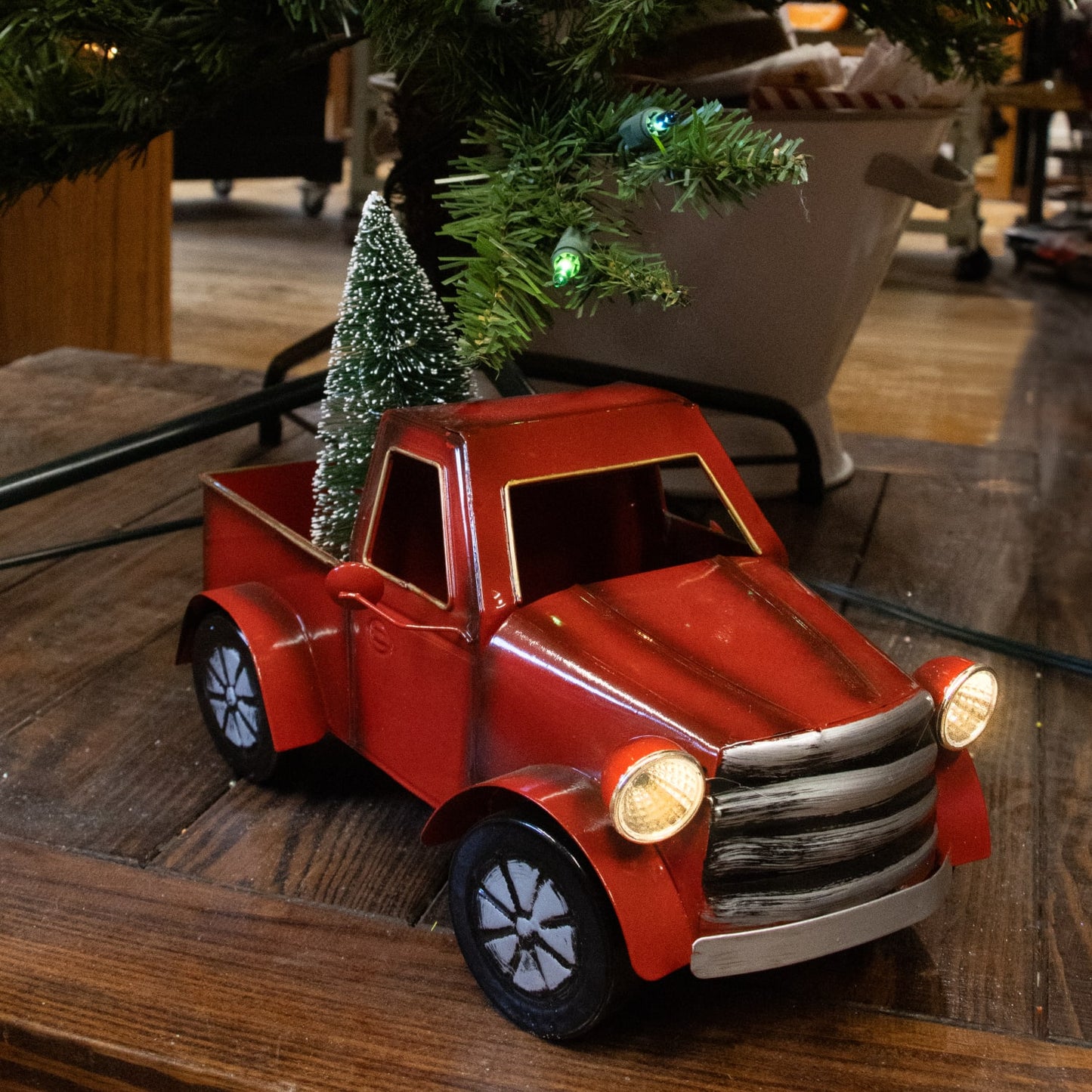 Small handcrafted red metal vintage-style holiday truck with battery-operated illuminated headlights and festive green tree in its bed, ideal for Home & Decor and Holiday Decor.