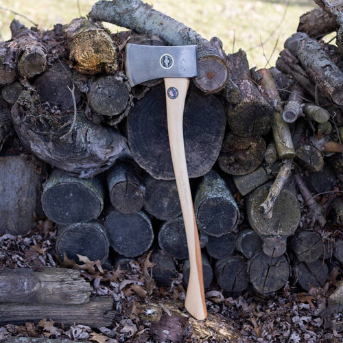 Handcrafted single bit axe with smooth hickory handle and high carbon steel head, leaning against stacked firewood, Amish made in USA, ideal for farm and wood cutting tasks.