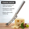 Serrated cheese knife with stainless steel blade and forked tip slicing through Swiss cheese with grapes and herbs nearby, a handcrafted USA made kitchen tool ideal for cheese and food prep.